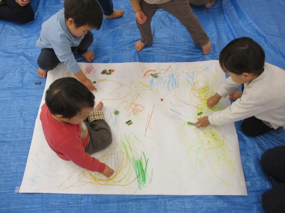 1歳児が大きな紙にクレヨンを使って絵を描いている