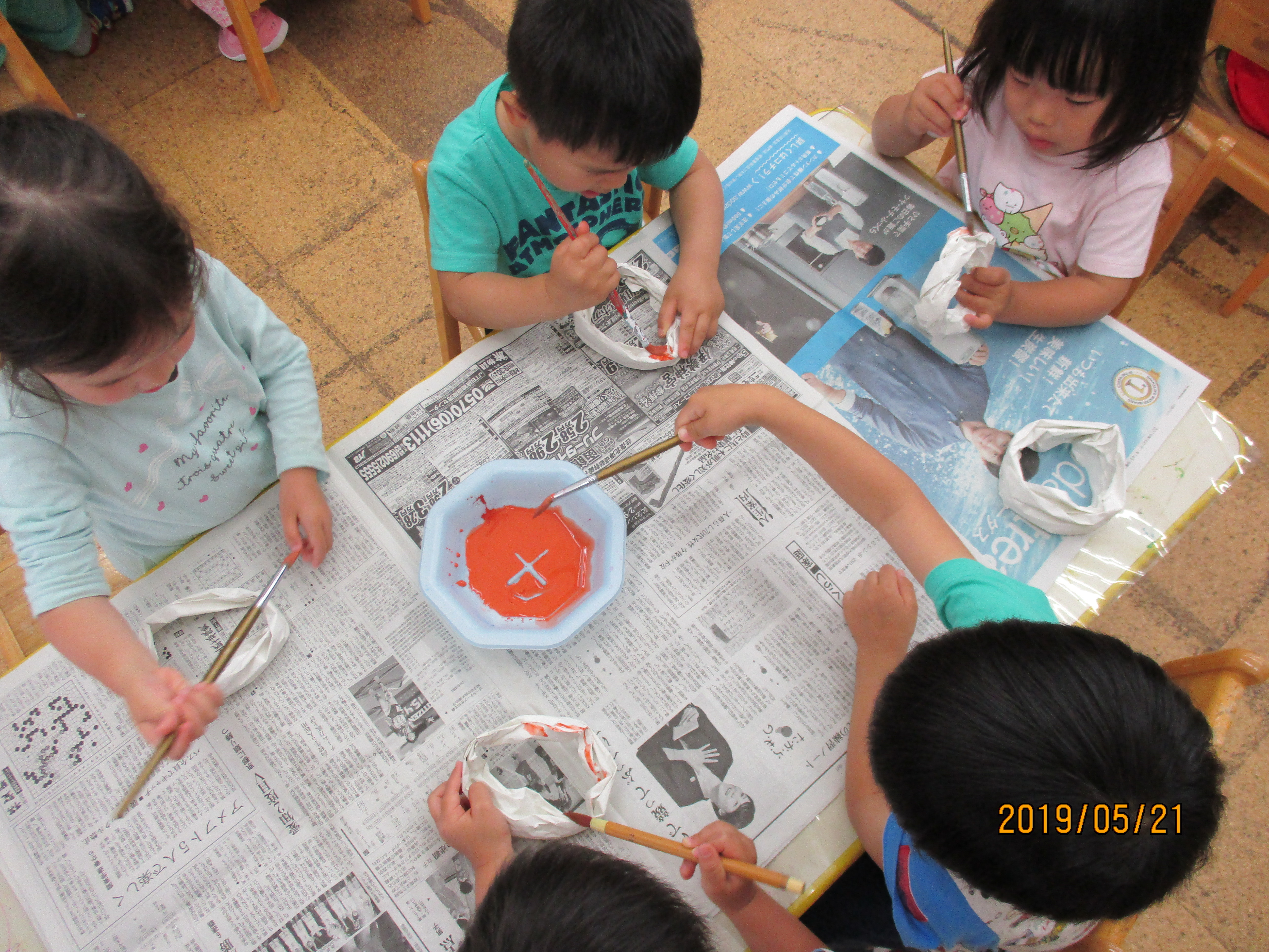 子ども達が紙で作ったドーナッツに、絵筆を使って絵の具で色を塗っています。