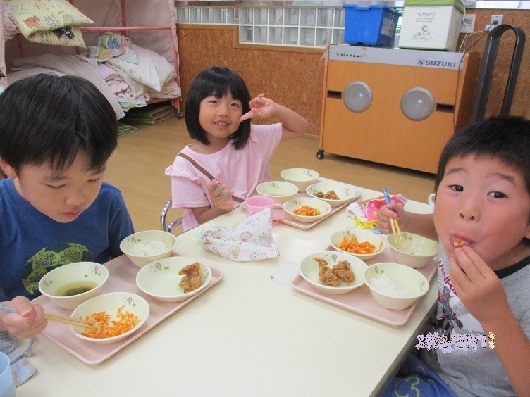 給食の時間。5歳児がリクエストした鶏の唐揚げ、人参しりしりが提供され、「おいしいね！」と笑顔で食べている。