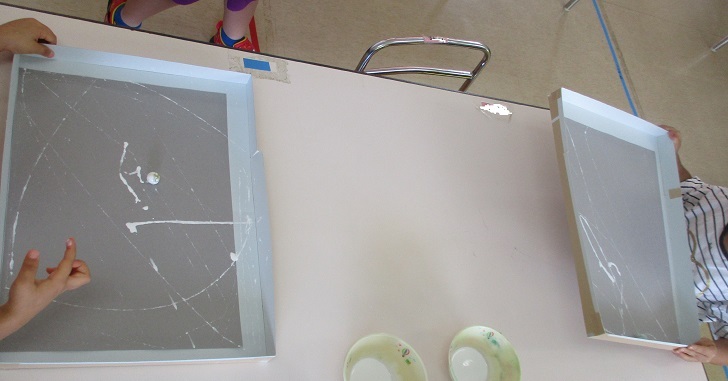 3歳児が絵の具を付けたビー玉を画用紙の上で転がし、模様を描いている。