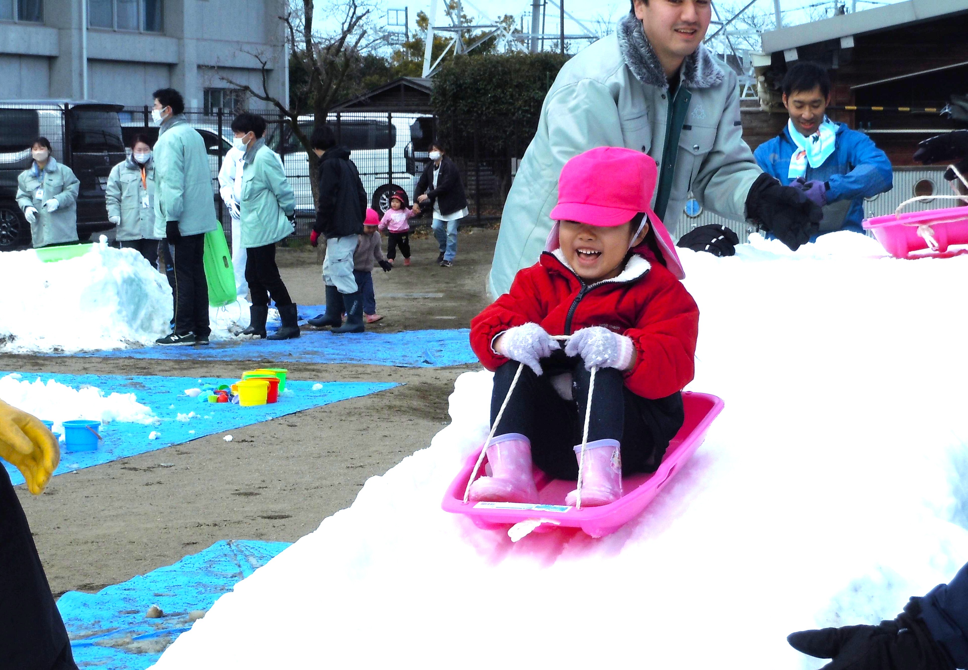 子どもがそりに乗り、雪で作った大きな滑り台を滑っている