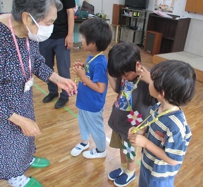 サロンの方が折り紙で作ったメダルを子どもたちの首にかけている。