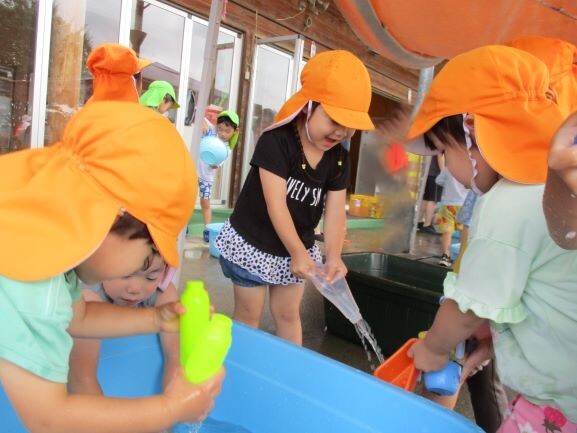 子どもが容器に水を入れ、笑顔で掛けあっている。