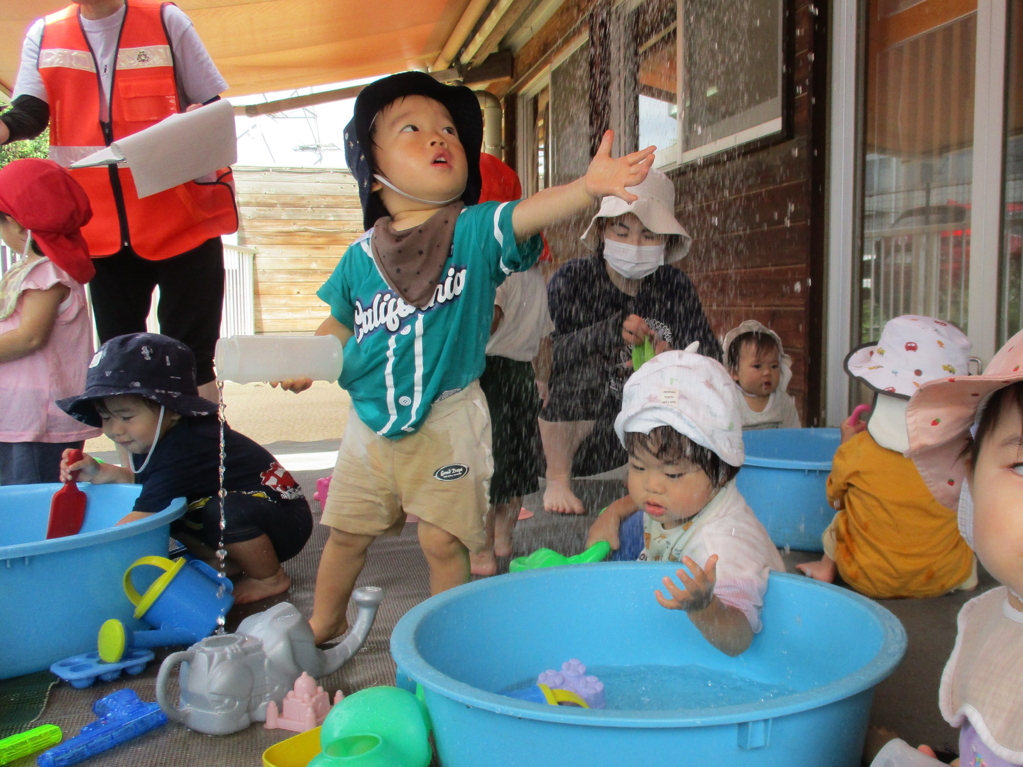 頭上から降り注ぐシャワーの水に、子どもが手を伸ばしている。