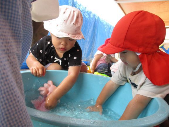 小さな子どもたちが、タライの水に手を伸ばし、感触を楽しんでいる。