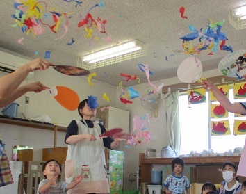 ちぎったお花紙を団扇で仰ぎ、花吹雪を楽しんでいる。