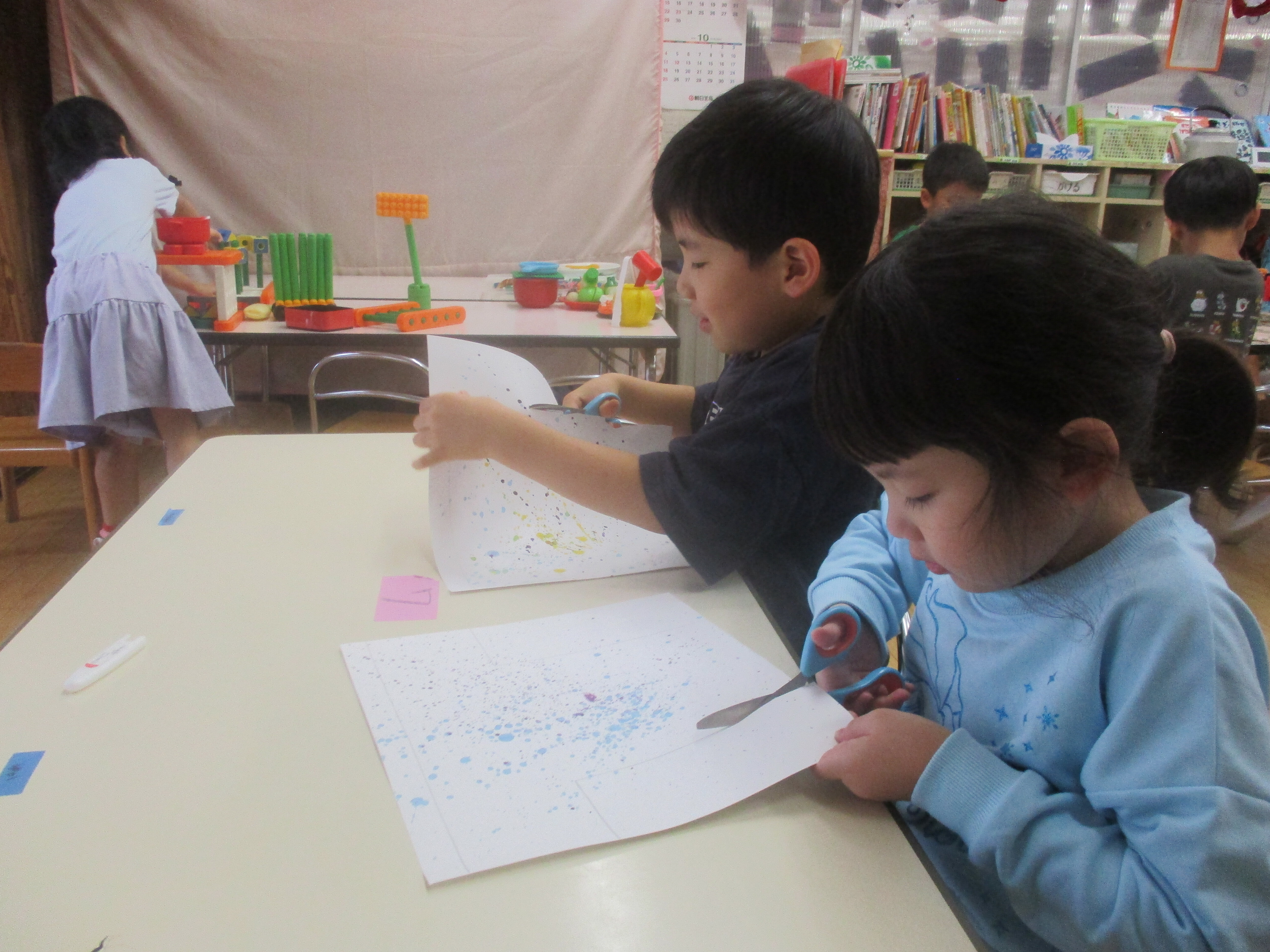 子どもたちが並んで座り、ハサミで形を切り取っている。