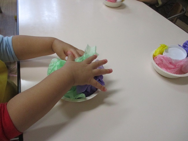 1歳児がおはながみを丸めて紙皿にのせている。