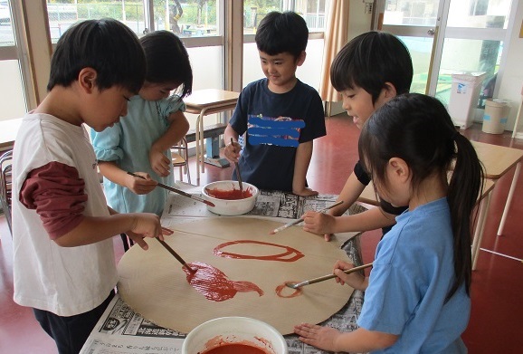 5歳児たちがダンボールに絵の具で色を塗っている。